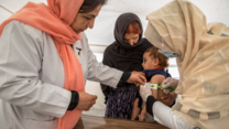 Three women hold a girl who is being screened for signs of malnutrition.