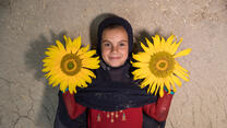 A girl stands holding two sunflowers