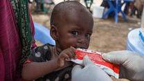 A baby in Somalia who is being treated for malnutrition eats specially nutritious peanut paste from a packet