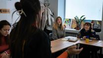 Drei Ukrainerinnen sitzen in einem Klassenraum, ihre Englischlehrerin ist mit dem Rücken zur Kamera gedreht