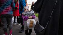 A young girls stands in a crowd, holding a blanket distributed by the IRC.