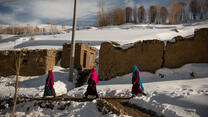 People walking across a snow-coated landscape in Afghanistan