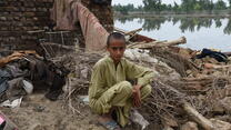 A young Pakistani boy sitting in front of his home ruined by floods