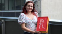 A woman stands holding a red and yellow box.