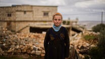 Girl stands in front of family home that has been devastated by an airstrike.