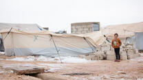 Little girl standing in front of her family's makeshift tent in a refugee camp in Syria.