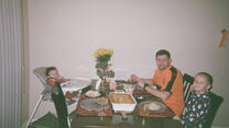 Evgen and two sons sit at dining table, ready to eat