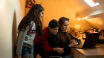 A woman sitting at a desk in front of a laptop, and two children standing next to her