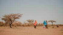 Two women walk through a drought-stricken landscape from Ethiopia. The barren landscape is dotted by dried-up trees.