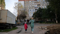 A mother and her child walk home past a crater caused by a missile strike.