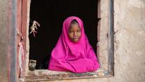 A girl poses for a picture while leaning out of a window sill.