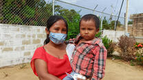 A mother holds her son and the pair pose for a photo outdoors.