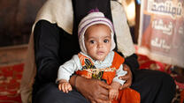 A young Yemeni child is held by their parent.