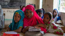 Maryama sits with two friends at a desk in class.