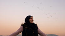 Ala is pictured against a backdrop of the sky and birds.