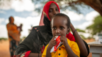 A young boy in Somalia receives a treatment for malnutrition in the form of a peanut-based paste. He eats the treatment food as he mother watches on.