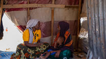 An IRC staff member consults a mother and her child inside a small building in a camp for internally displaced Somalis. The pair share a conversation while sitting on the floor.