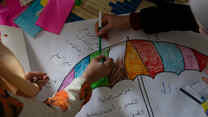 Syrian refugee girls color and write on a piece of paper on the floor in the safe space where they take part in different kind of activities with the IRC WPE team.