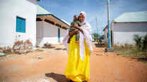 Fartun stands in the street, holding her baby son.