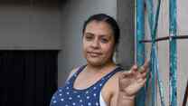 A Honduran woman poses for a portrait photo next to a blue gate.