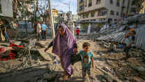 En mamma går med sitt barn genom ruinerna efter israeliska luftangrepp i Gaza den 7 oktober 2023.