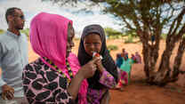 IRC staff with young girl eating PlumpyNut in Olol Village, Somalia