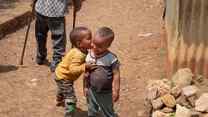 Two young children in Ethiopia embrace outside. They smile together.