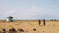 Two women walk away from the camera. In the background lies a barren Ethiopia landscape, dotted by an IRC-supported water facility.