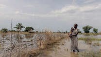 Abuk, holding Nyirou, poses for a portrait in front of their flooded house, in Northern Bahr El Ghazal, South Sudan.