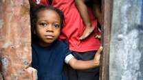 A young girl stands in a doorway in Haiti, looking at the camera