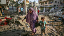 A woman and child pick their way through the rubble after an airstrike hits Gaza City.