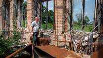 A middle-aged man walks through the ruins of a destroyed building.