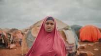 Amina, a refugee living in Somalia, standing in front of an internally displaced persons camp