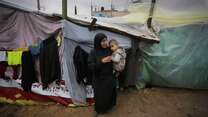 A woman holds a young child outside a makeshift shelter in Gaza.