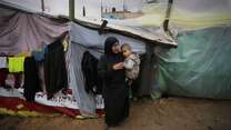 가자 지구의 임시 대피소 밖에서 한 여성이 어린 아이를 안고 있습니다.