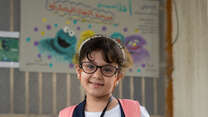 A girl in a classroom smiles and poses for a portrait.