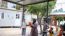 Menschen stehen unter einem Pavillon im Freien, umgeben von Bäumen und Gebäuden.