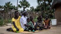 Frau mit Kindern sitzt auf einer Matte vor einem Haus in Südsudan.