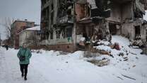 A woman walks down a snow-covered street in Ukraine, beside a building that has been destroyed in the war/