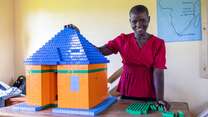 Girl stands next to a house made from Lego bricks
