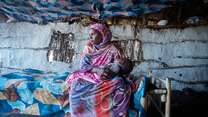 A mother holds her young child in her arms. The two are inside of a makeshift shelter in Sudan.