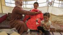 A mother and her two children try on new winter clothes they received from the IRC.