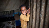 Kindesa (3) lächelt, als er die Tür seines Zuhauses im Geflüchtetenlager für Binnenvertriebene in Deder, Äthiopien, öffnet.