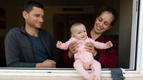 En pappa och mamma håller i sin fem månader gamla dotter vid ett fönster.