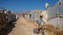 A boy rides a bike at a camp for displaced people in Lebanon.