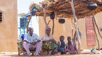 Bila Natama sitzt mit ihren Töchtern und ihrem Mann unter einem Unterstand vor ihrem Grundstück in Tibga, Burkina Faso 