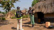 Martin greets Elizabeth, who is holding her young child during a home visit. For many families in the settlement, a knock at the door from Martin is the first step toward getting care.