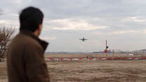 A man looks on as a plane takes off at an airport.