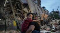 A person carries a child in front of a pile of rubble and destroyed buildings after an earthquake in Venezuela.