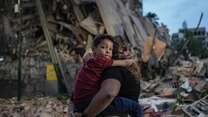A person carries a child in front of a pile of rubble and destroyed buildings after an earthquake in Venezuela.